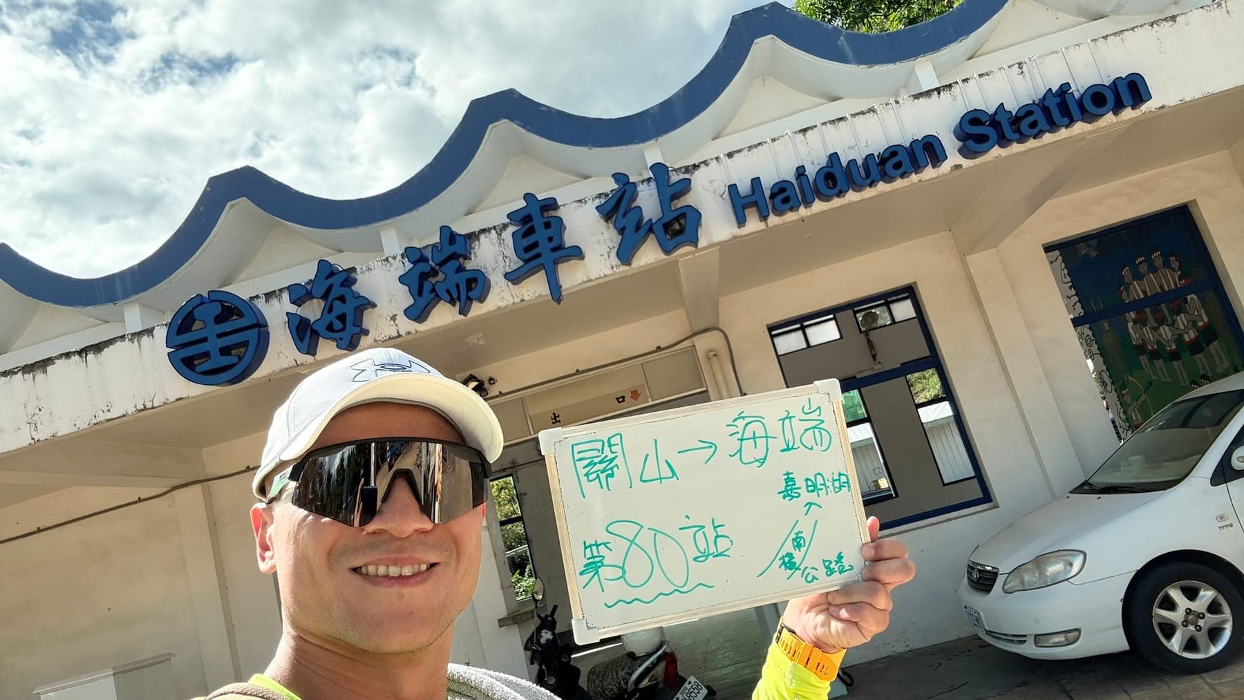 站主在海端站站牌前的走訪紀錄照，手持寫著「徒步環島 第 80 站　關山 → 海端」的白板