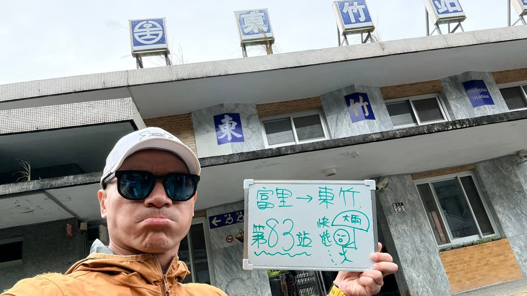 站主在東竹站站牌前的走訪紀錄照,手持寫著「徒步環島 第 83 站 富里 → 東竹」的白板