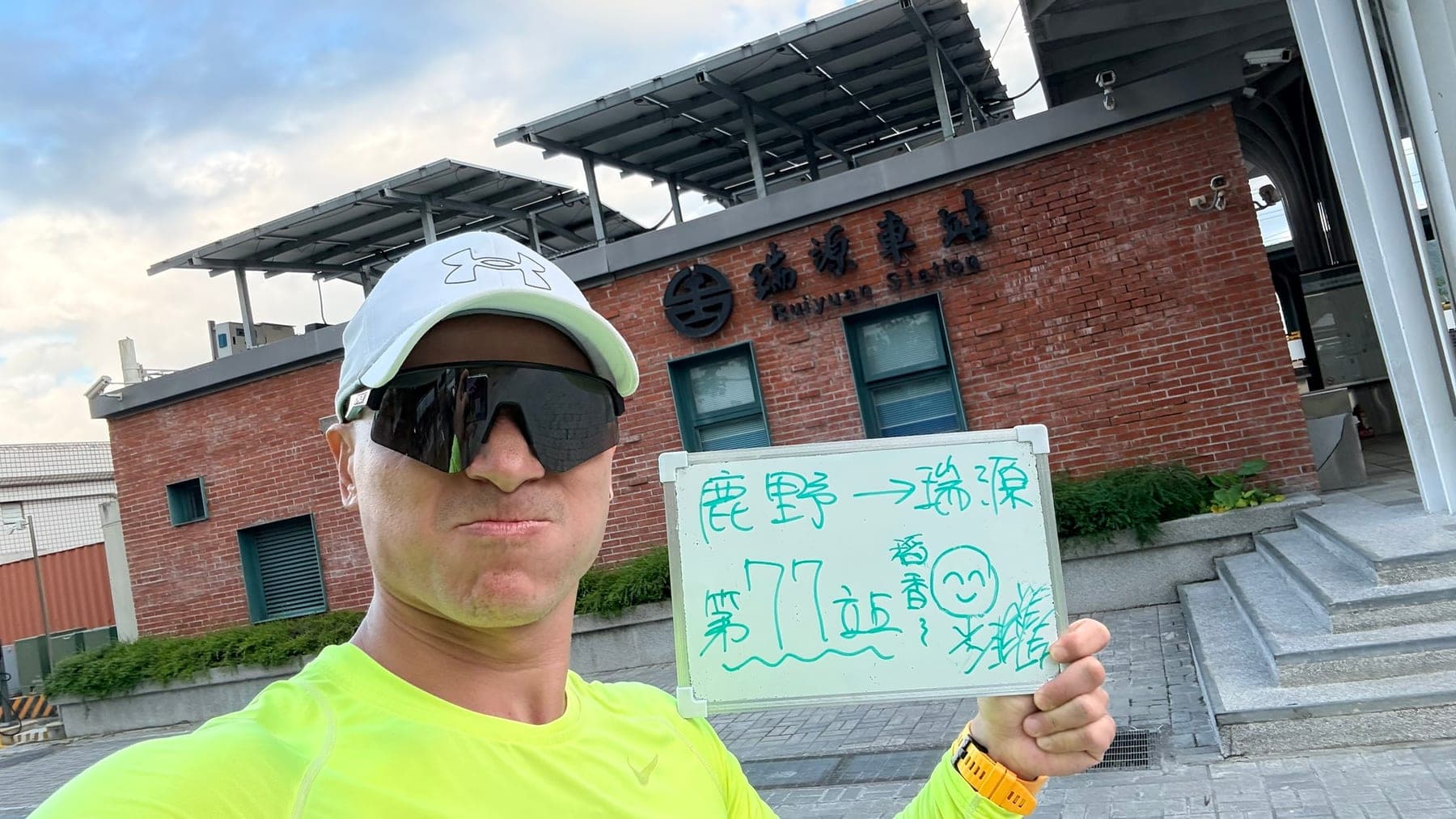 站主在瑞源站站牌前的走訪紀錄照,手持寫著「徒步環島 第 77 站 鹿野 → 瑞源」的白板