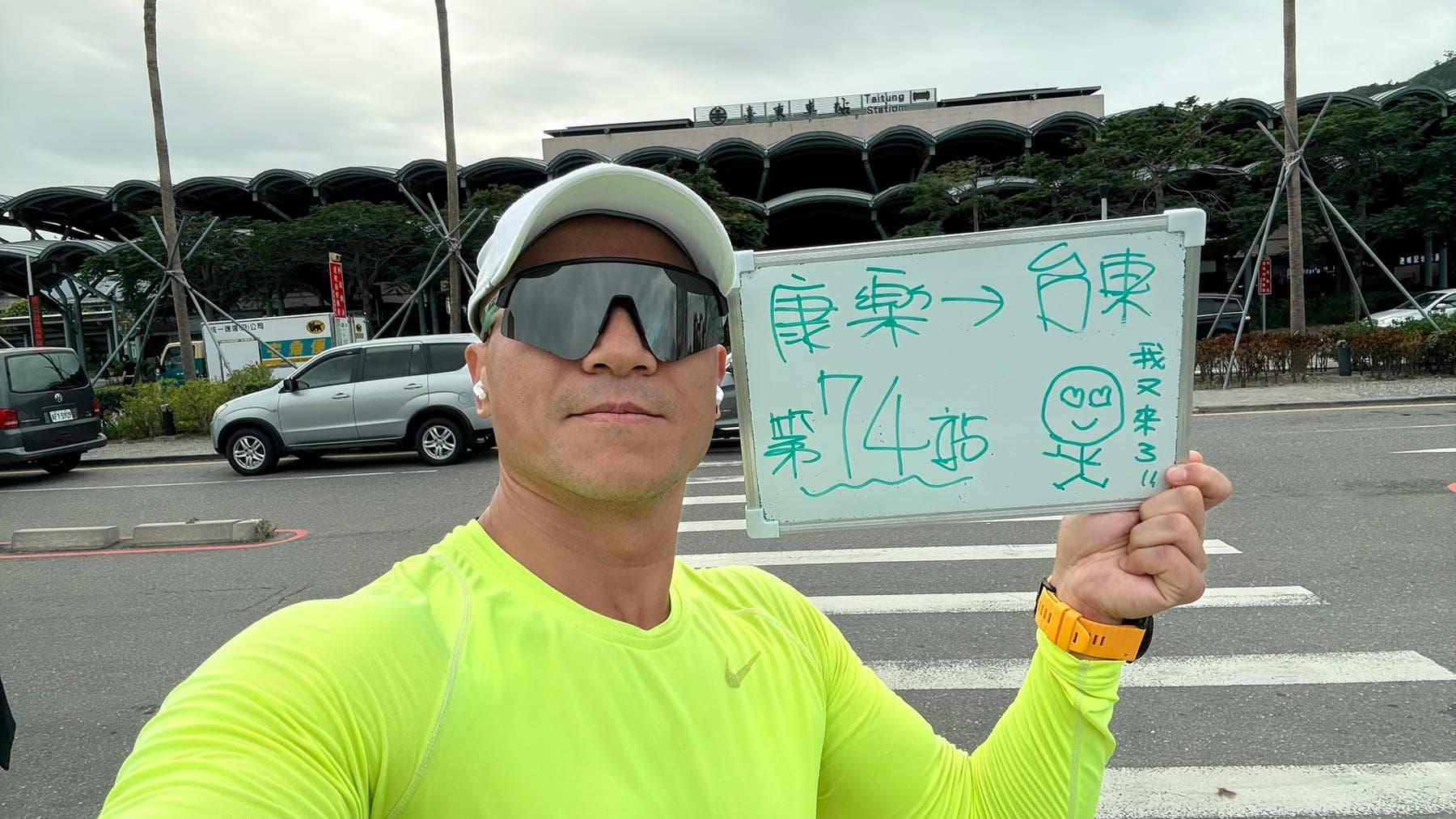 站主在台東站站牌前的走訪紀錄照,手持寫著「徒步環島 第 74 站 康樂 → 台東」的白板