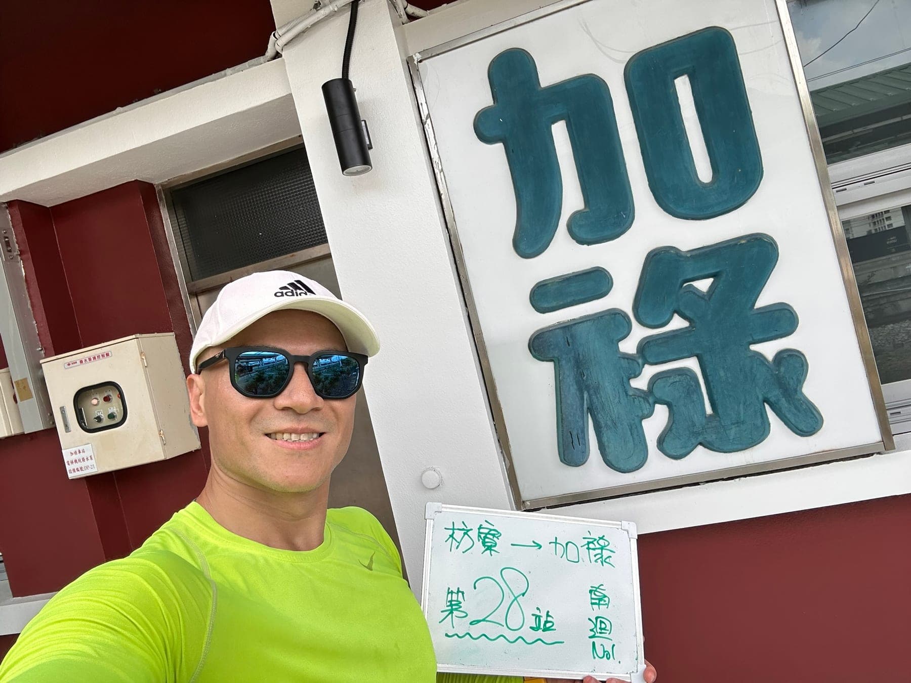 站主在加祿站站牌前的走訪紀錄照,手持寫著「徒步環島 第 28 站 枋寮 → 加祿」的白板
