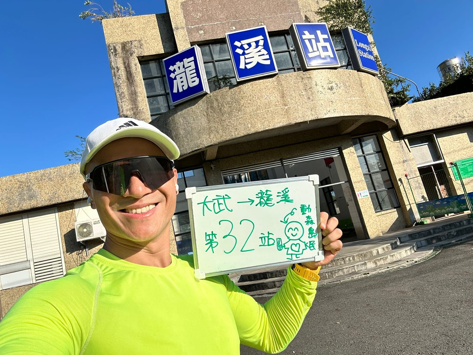 站主在瀧溪站站牌前的走訪紀錄照,手持寫著「徒步環島 第 32 站 大武 → 瀧溪」的白板