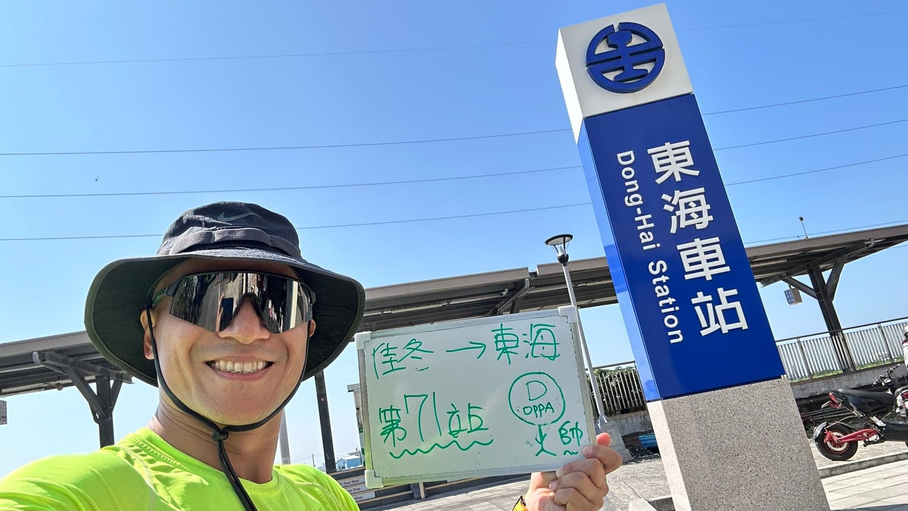 站主在東海站站牌前的走訪紀錄照,手持寫著「徒步環島 第 71 站 佳冬 → 東海」的白板