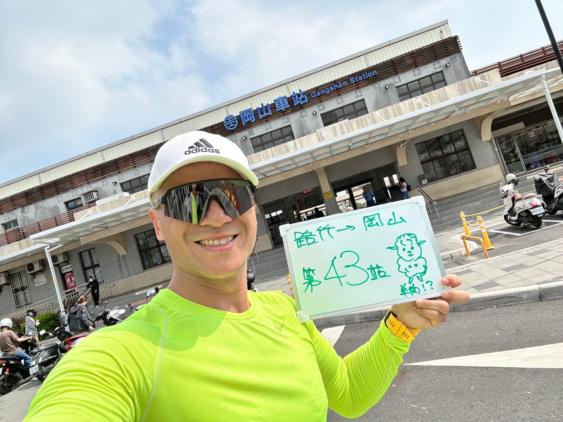 站主在岡山站站牌前的走訪紀錄照,手持寫著「徒步環島 第 43 站 路竹 → 岡山」的白板