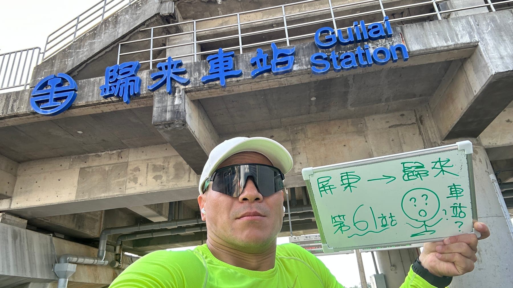 站主在歸來站站牌前的走訪紀錄照,手持寫著「徒步環島 第 61 站 屏東 → 歸來」的白板