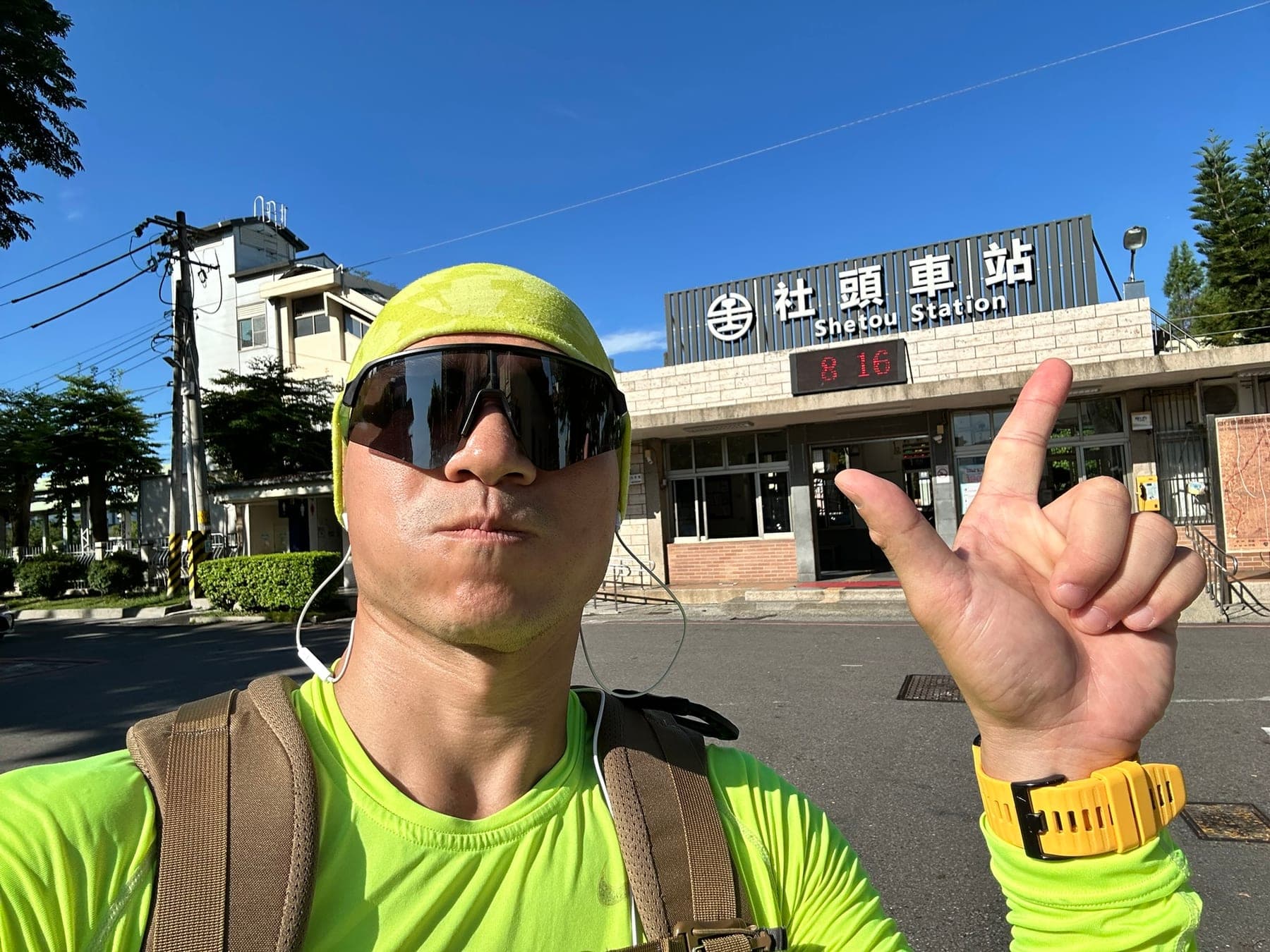 站主在社頭車站前的走訪紀錄照,手比二代表第 2 站,站房上方電子鐘顯示 8:16
