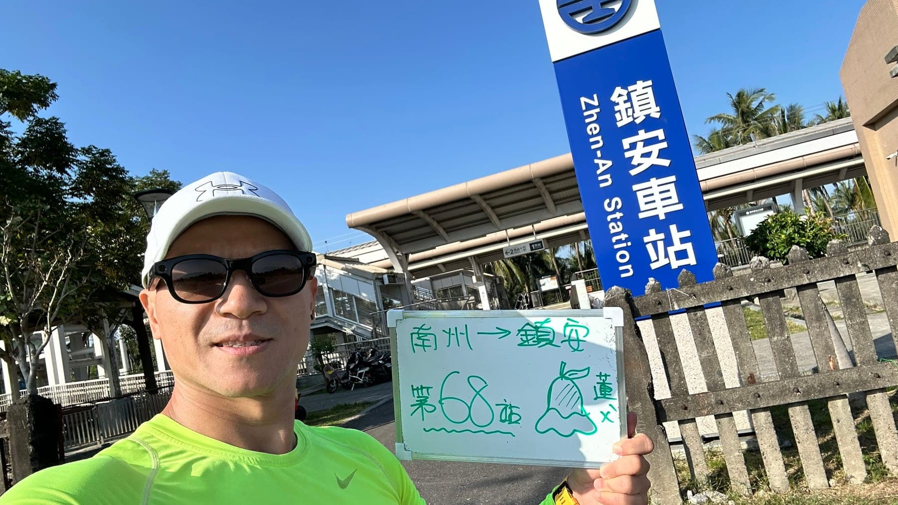 站主在鎮安站站牌前的走訪紀錄照,手持寫著「徒步環島 第 68 站 南州 → 鎮安」的白板